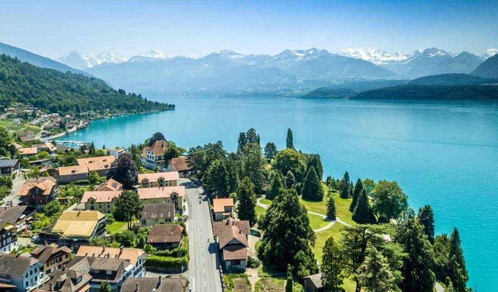 A picture of Switzerland with houses in the foreground and a lake and mountains in the background